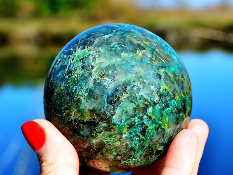Large chrysocolla sphere 85mm on hand with river landscape background