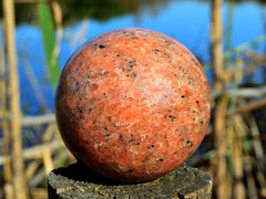 One big orange calcite sphere mineral 85mm on a wood log on river landscape background