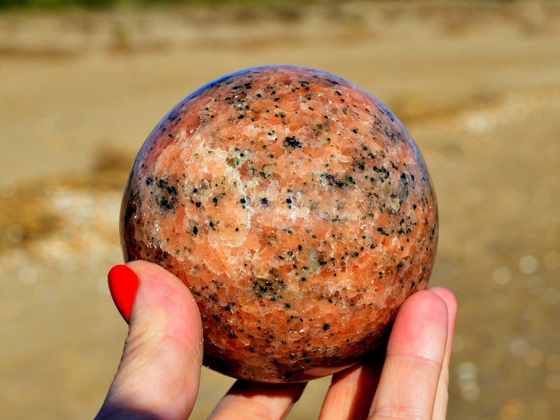 Big orange calcite crystal sphere 65mm on hand with sand background
