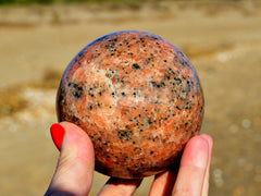 Big orange calcite crystal sphere 65mm on hand with sand background