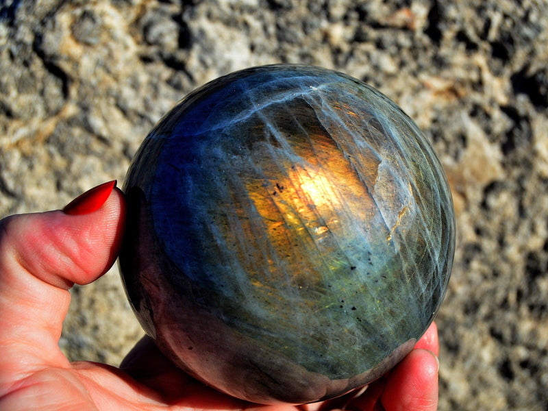 One large flash labradorite crystal ball 85mm on hand with rock background