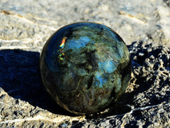 One large labradorite sphere 75mm on hand with rock background