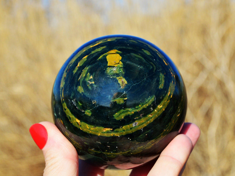 One green and yellow ocean jasper mineral sphere 65mm on hand with wild straw background