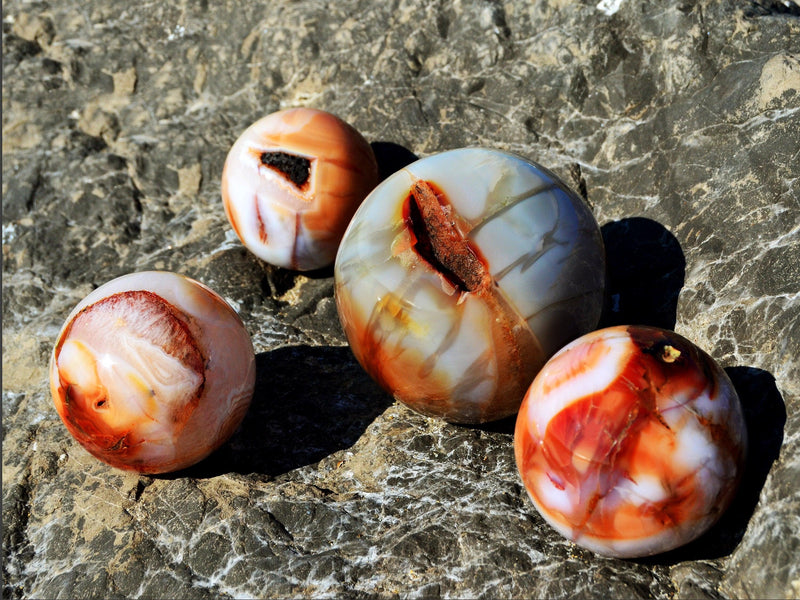 Four natural carnelian sphere minerals 70mm-100mm on natural rock background