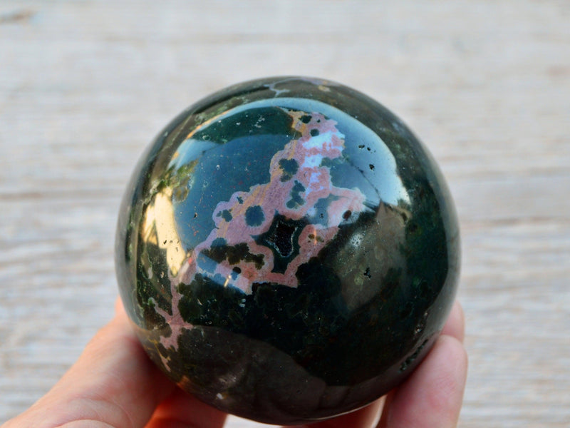 One green and pink ocean jasper sphere crystal 85mm on hand with wood background