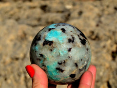 One green amazonite ball 70mm on hand with rock background