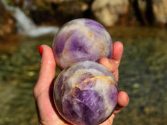 Two amethyst crystal balls on hand with river landscape