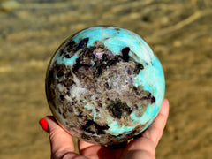 One green amazonite sphere 95mm on hand with background with river landscape