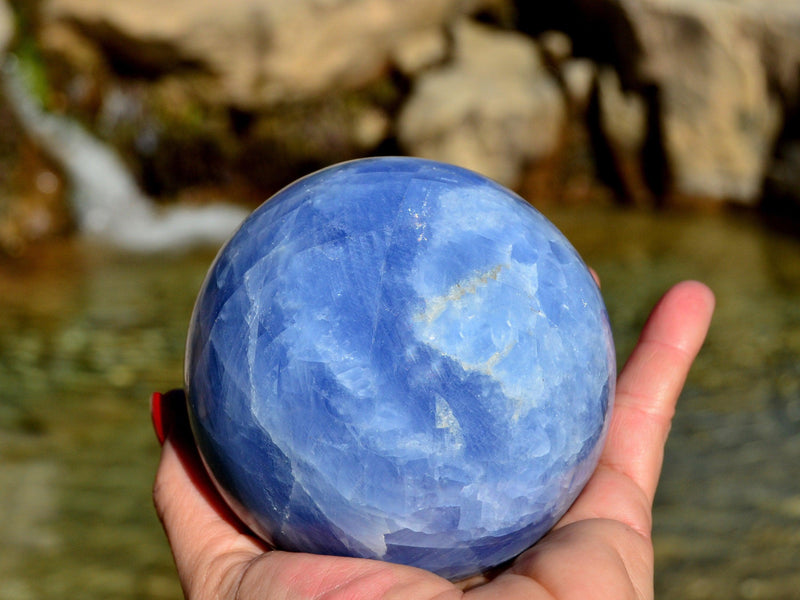 Large blue calcite crystal sphere 90mm on hand with river landscape