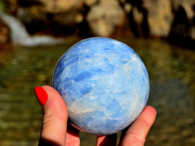 Large blue calcite sphere 70mm on hand with river landscape