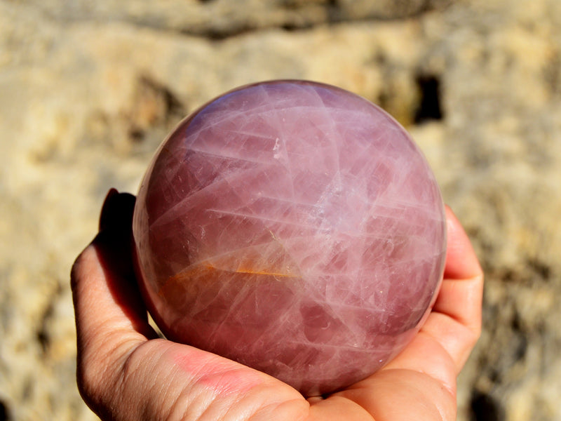 One large rose quartz crystal sphere 90mm on hand with rock background 