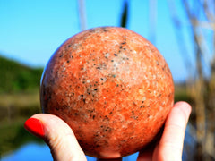 Big orange calcite crystal sphere 90mm on hand with river landscape background