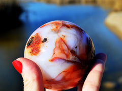 One natural carnelian crystal ball 80mm on hand with river landscape background