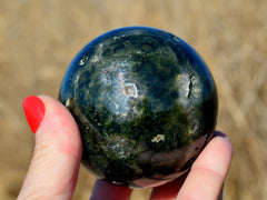 One green ocean jasper mineral sphere 65mm on hand with wild straw background