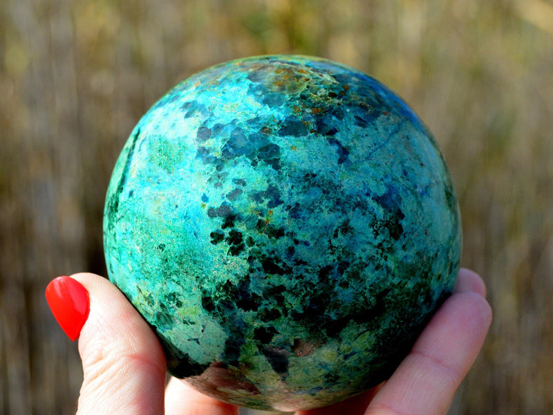 Large chrysocolla crystal sphere 90mm on hand with baackground with plants