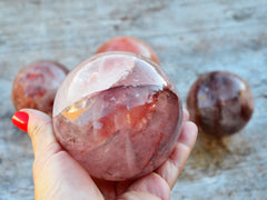 One large fire quartz minerals sphere 85mm on hand with background with some spheres on wood table