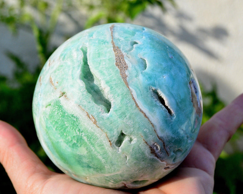 Large druzy blue aragonite ball 90mm on hand with background with green plants