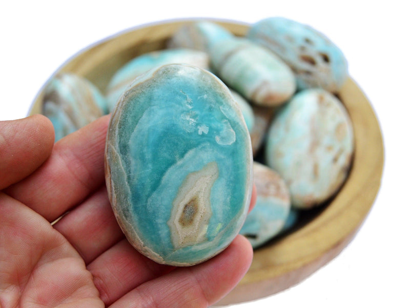 One blue aragonite palm stone 60mm on hand with background with some crystals inside a wood bowl