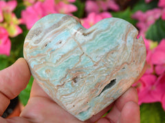 One large blue aragonite heart 85mm on hand with background with pink flowers
