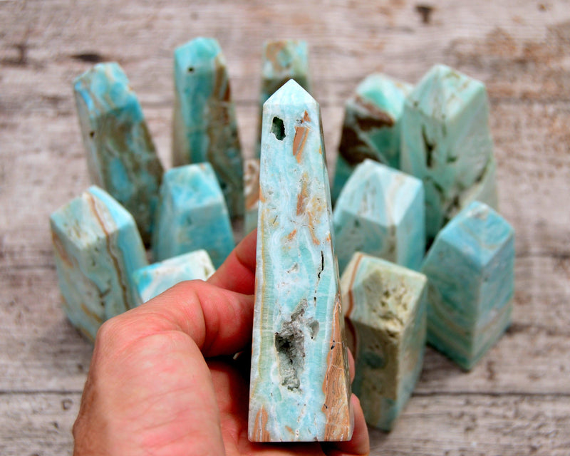 One blue aragonite tower on hand with background with several crystals on wood table