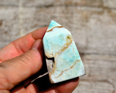 One small blue aragonite crystal tower on hand with wood background