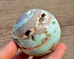 Druzy blue aragonite sphere 70mm on hand with wood background