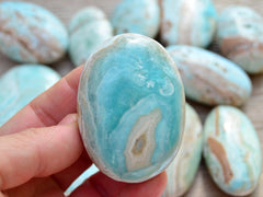 Blue aragonite palm stone 60mm on hand with background with some crystals on wood table
