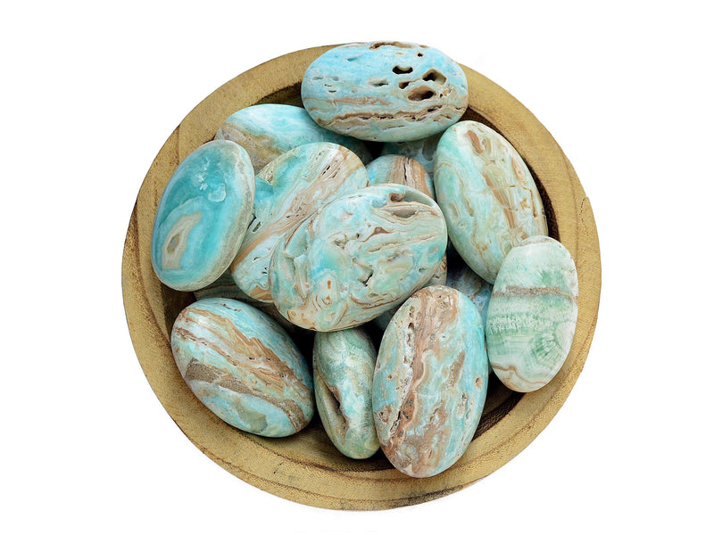 Several blue aragonite palm stones inside a wood bowl on white background