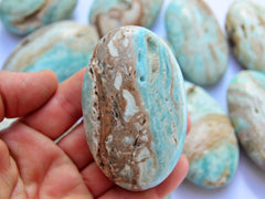 One blue aragonite palm stones 80mm on hand with background with some crystals