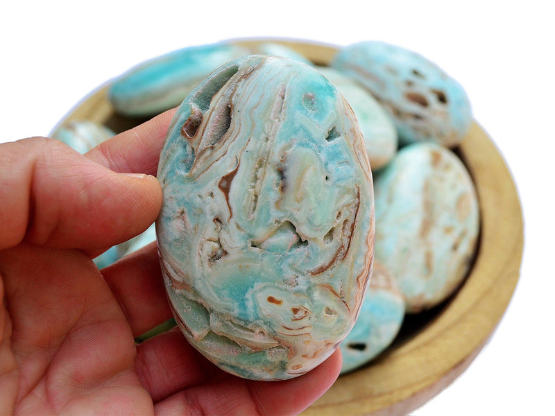 One blue aragonite palm stone 70mm on hand with background with some crystals inside a wood bowl