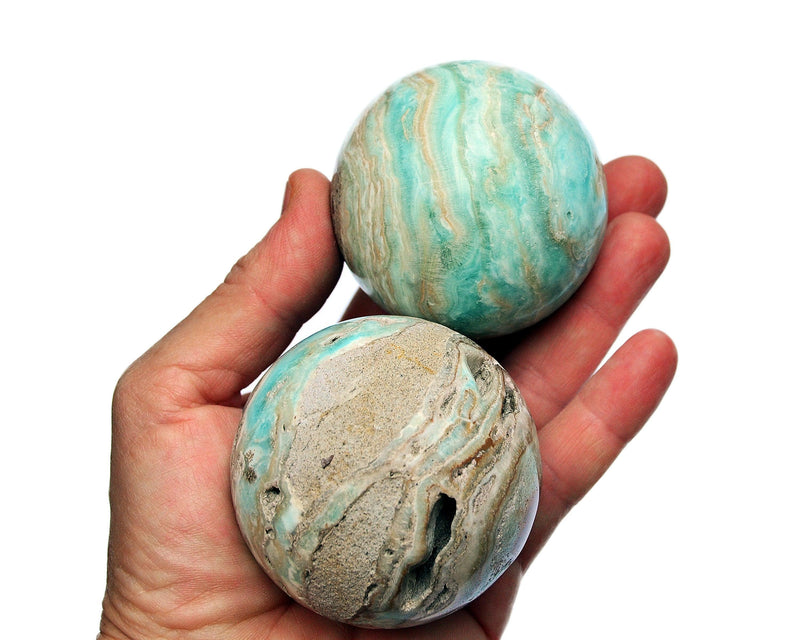 Two druzy blue green aragonite crystal spheres 55mm - 60mm on hand with white background