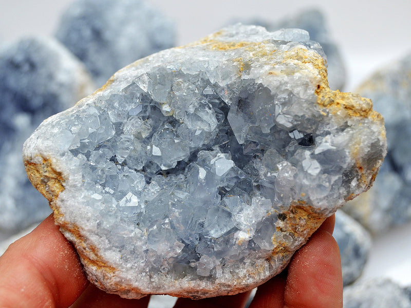 Large blue celestite crystal cluster 80mm on hand with background with some stones