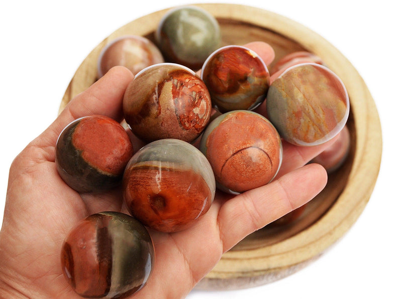 Polychrome jasper crystal sphere stones 25mm - 40mm on hand with background with some spheres inside a wood bowl