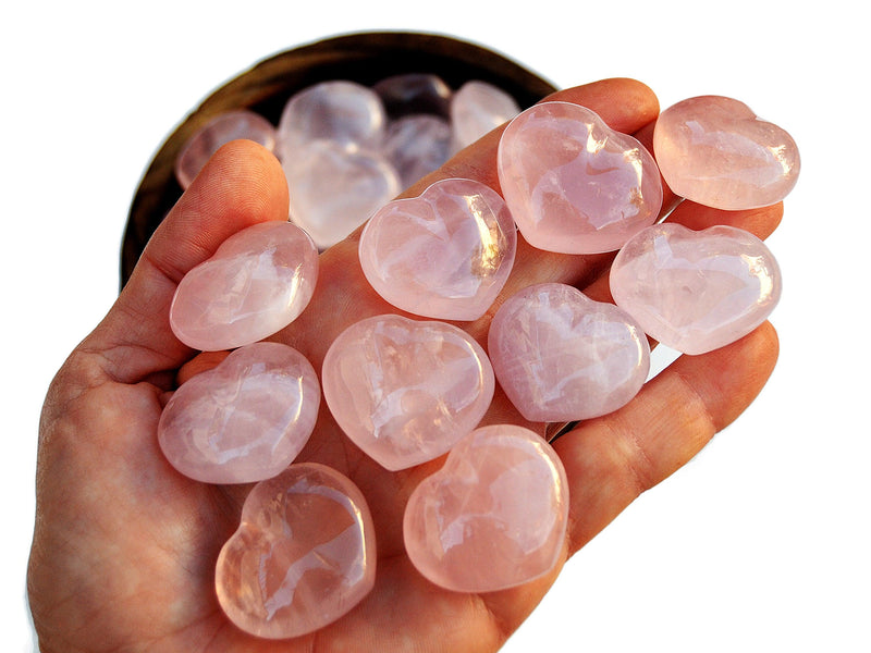 Ten rose quartz puffy heart crystals 30mm on hand with background with some hearts insde a bowl