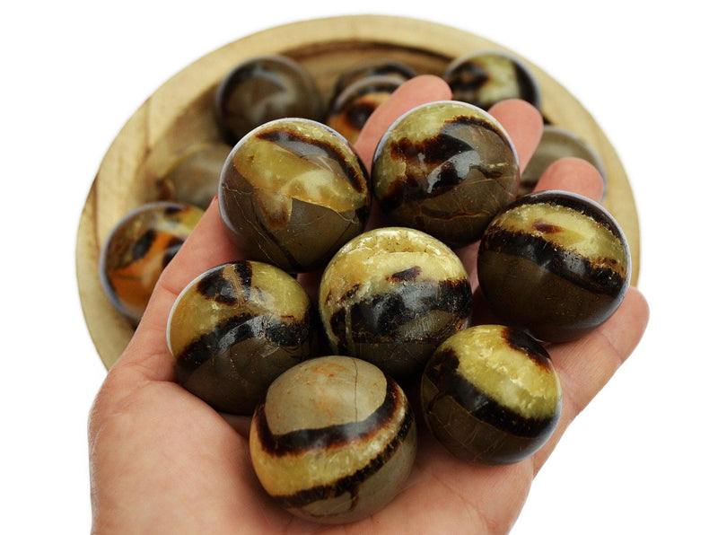 Several yellow septarian crystal spheres 25mm - 40mm on hand with background with some stones inside a wood bowl